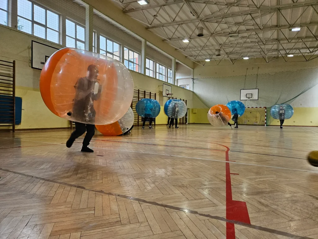Drużyny w pomarańczowych i niebieskich kulach bumper ball na hali