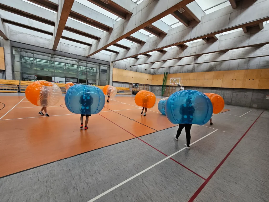 Drużyny w pomarańczowych i niebieskich kulach bumper ball na hali