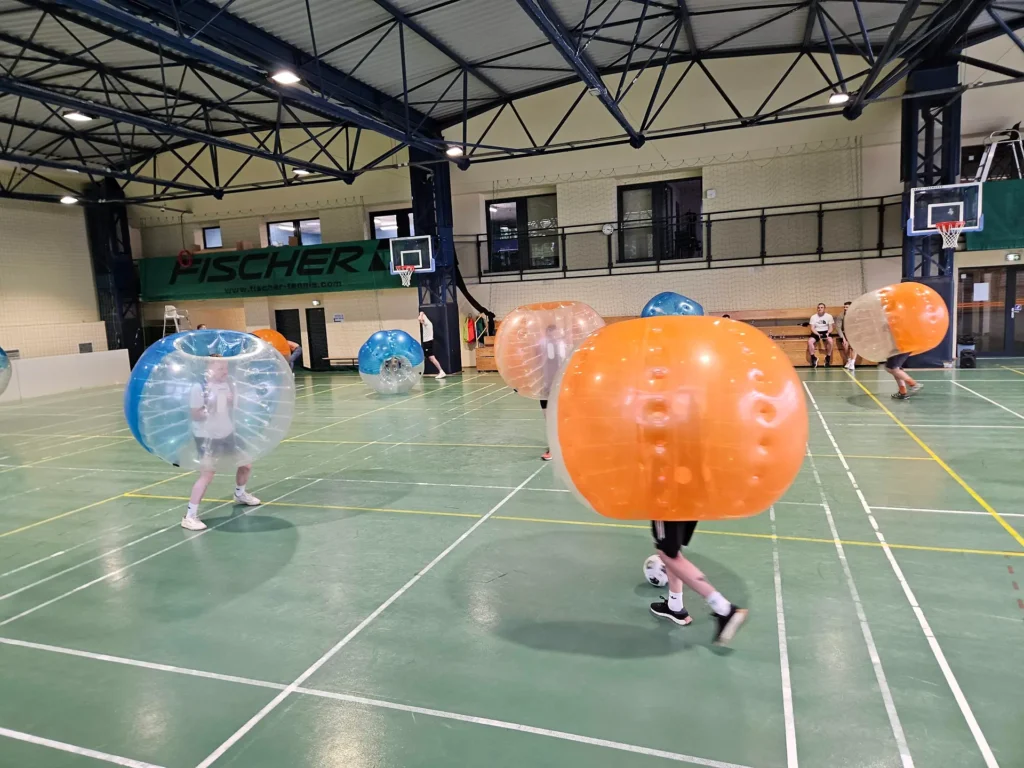 Drużyny w pomarańczowych i niebieskich kulach bumper ball na hali