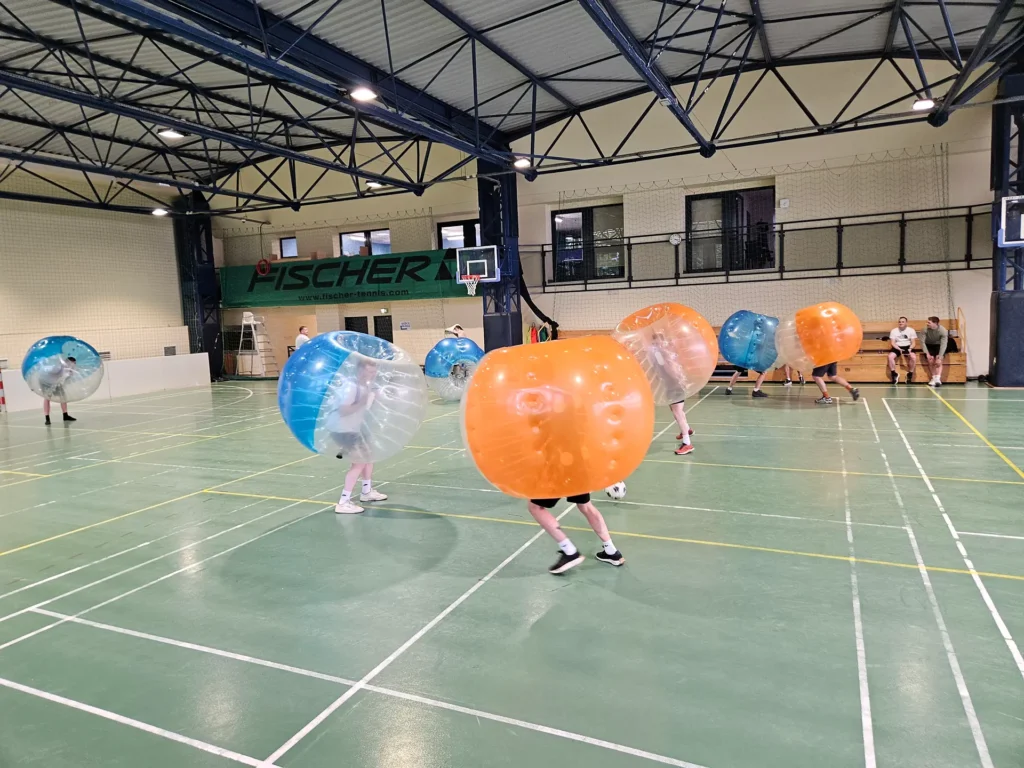 Drużyny w pomarańczowych i niebieskich kulach bumper ball na hali
