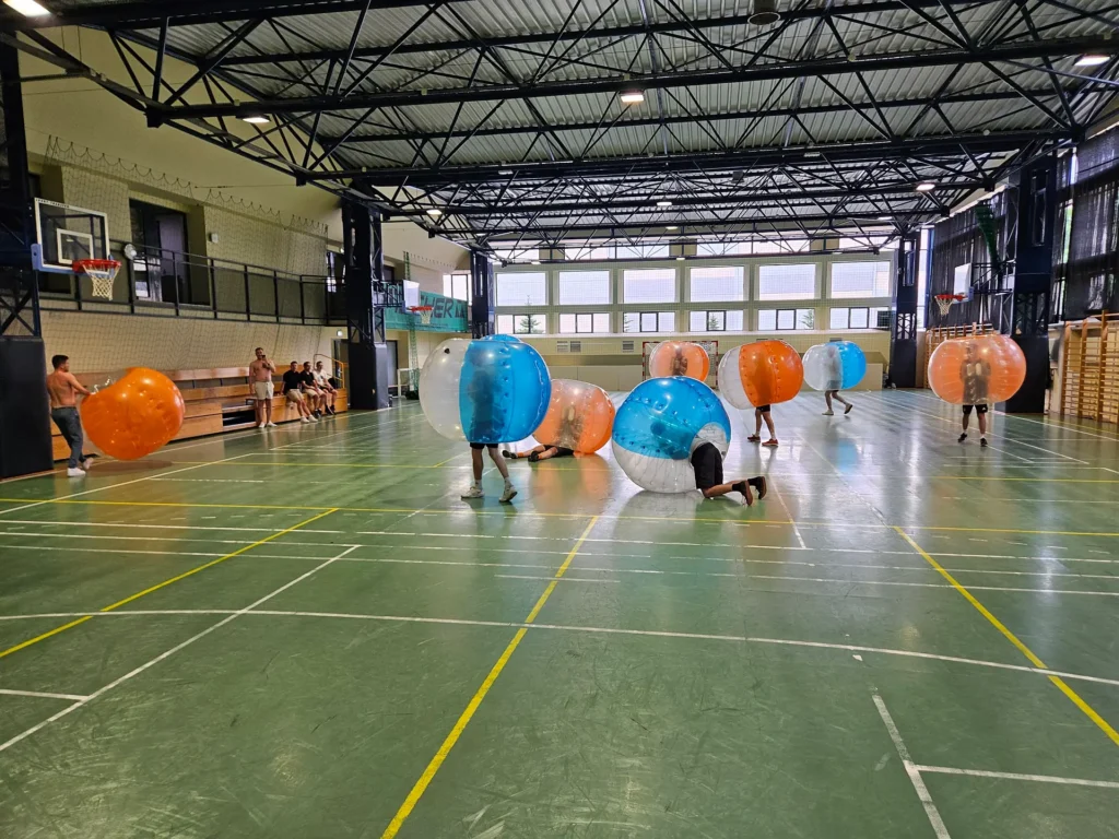 Drużyny w pomarańczowych i niebieskich kulach bumper ball na hali