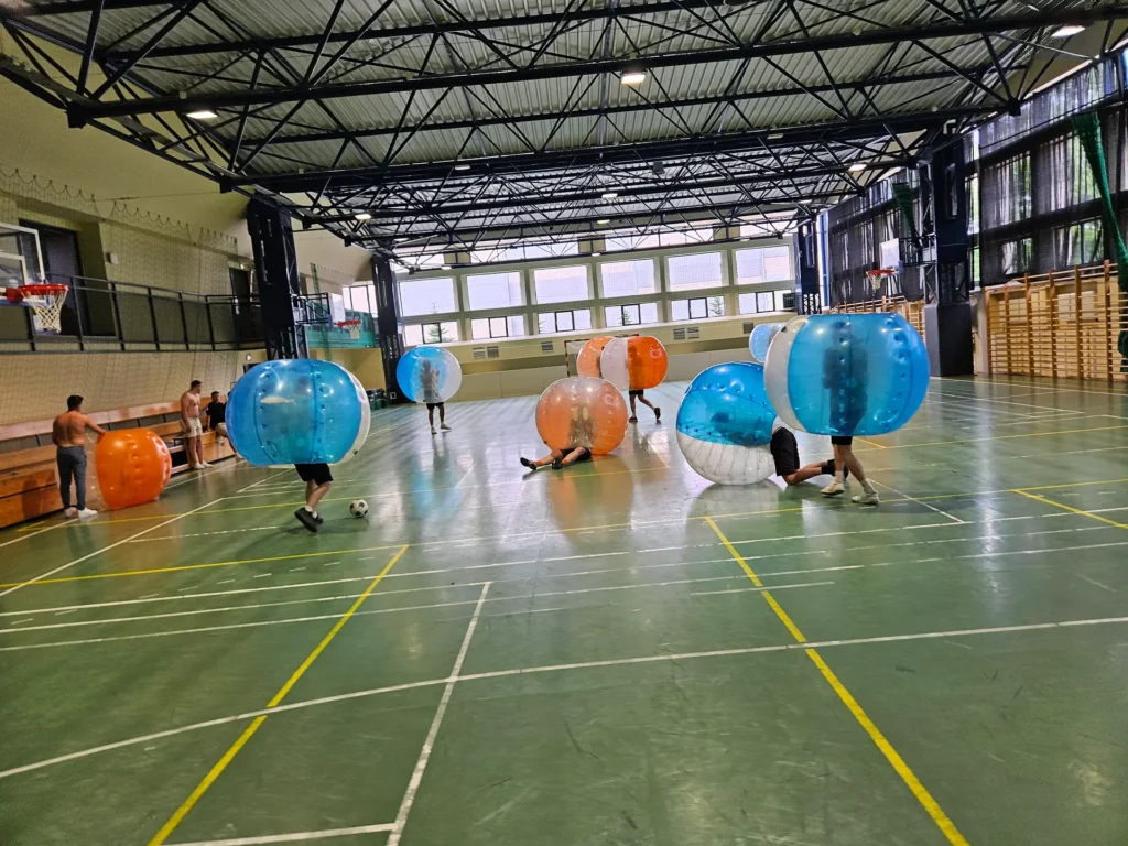 Drużyny w pomarańczowych i niebieskich kulach bumper ball na hali