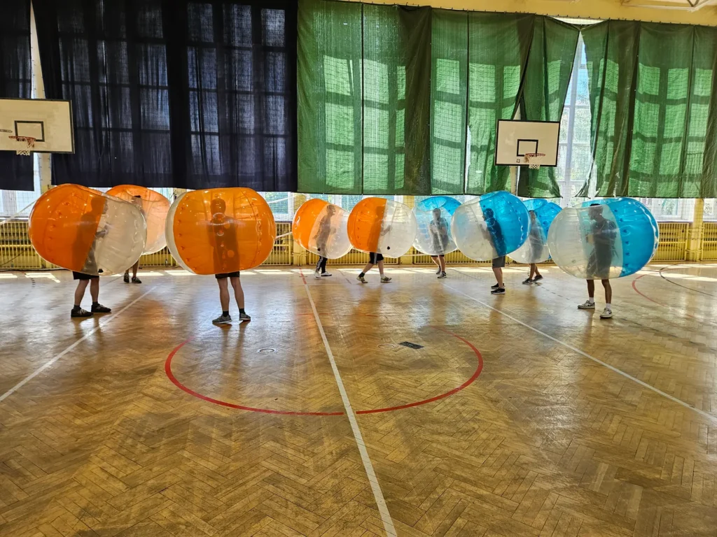 Drużyny w pomarańczowych i niebieskich kulach bumper ball na hali