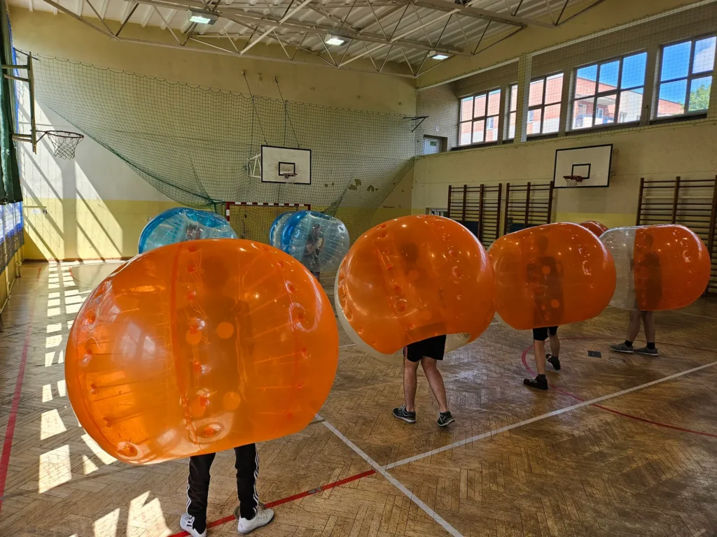Drużyny w pomarańczowych i niebieskich kulach bumper ball na hali