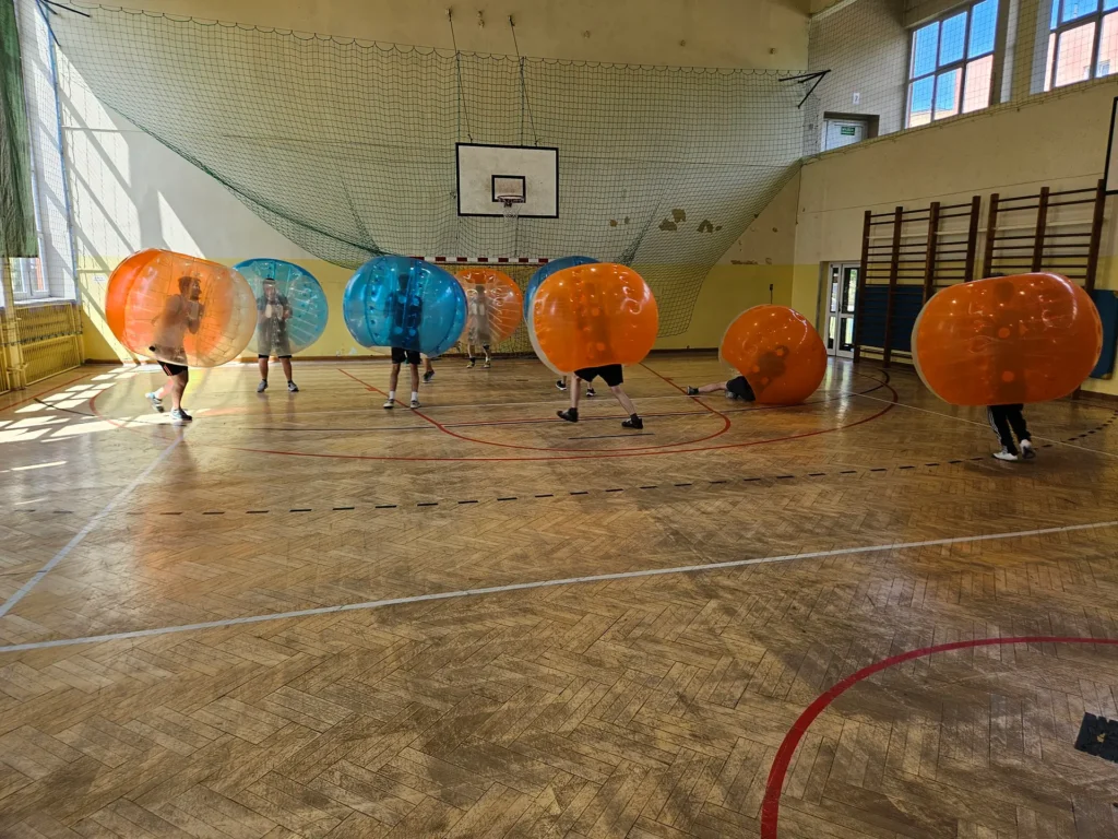 Drużyny w pomarańczowych i niebieskich kulach bumper ball na hali