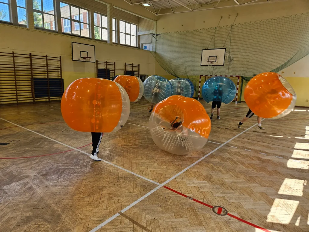 Drużyny w pomarańczowych i niebieskich kulach bumper ball na hali