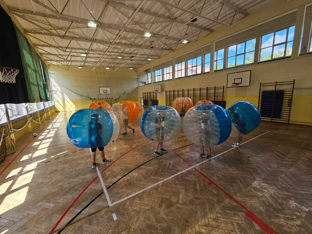 Drużyny w pomarańczowych i niebieskich kulach bumper ball na hali