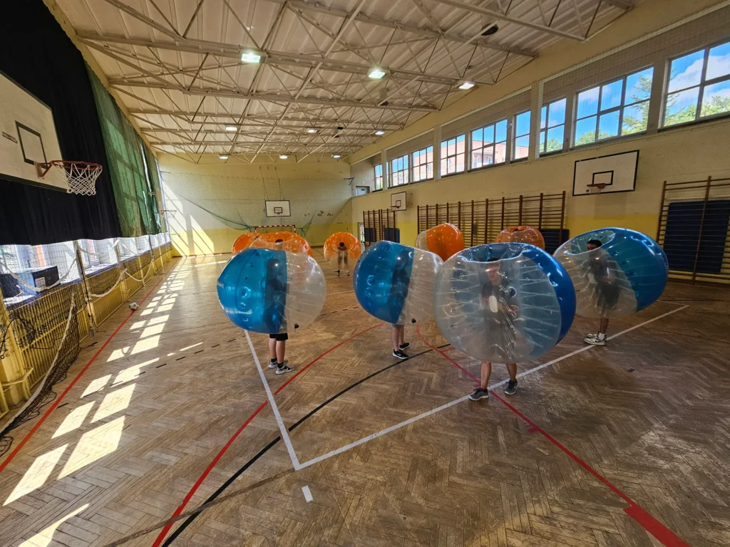 Drużyny w pomarańczowych i niebieskich kulach bumper ball na hali