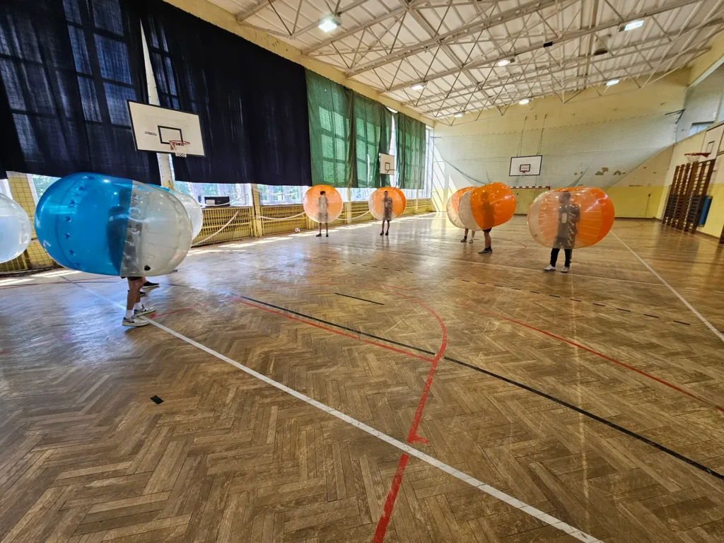 Drużyny w pomarańczowych i niebieskich kulach bumper ball na hali