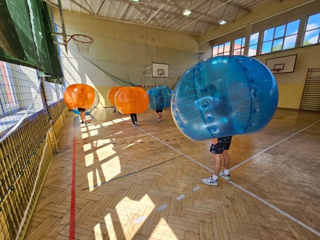 Drużyny w pomarańczowych i niebieskich kulach bumper ball na hali